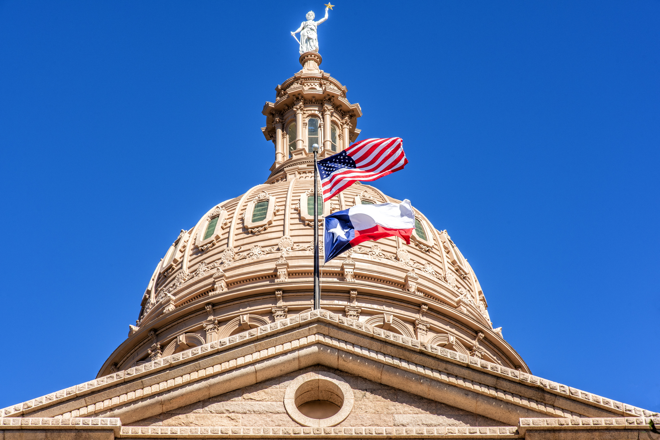 Dome of Texas State Capitol building with the U.S. flag and Texas flag waving in the foreground