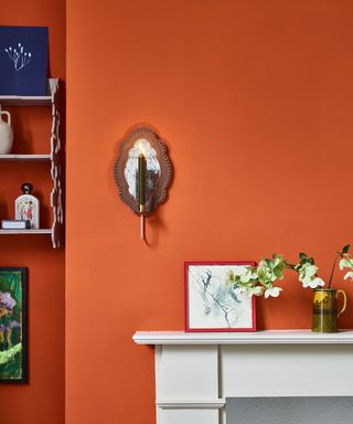 An orange wall with wall shelves and a white mantelpiece with decor on it