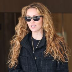 Miley Cyrus wearing a black tweed jacket, straight-leg jeans, and lug-sole boots