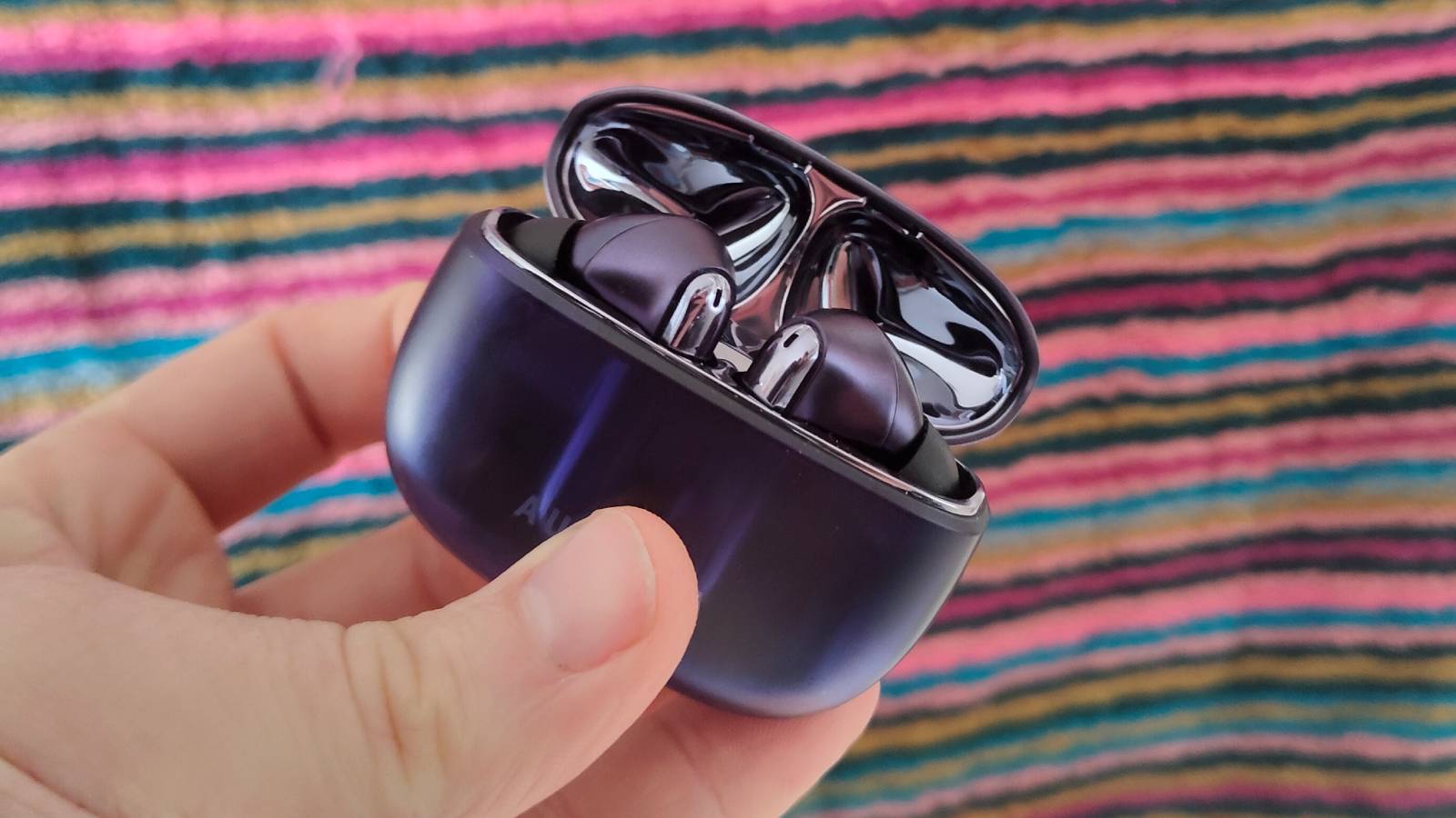 The Creative Aurvana Ace 3 buds and case in front of a stripy colorful screen.