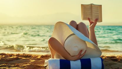 woman in a hat reading at the beach