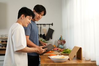 Two men are smiling and cooking a meal in the kitchen together.