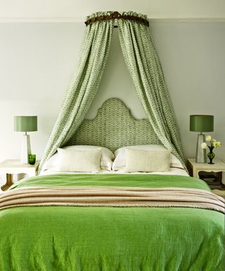 An example of green bedroom ideas showing a bed with green velvet throw and matching upholstered headboard and canopy in green and white patterned fabric