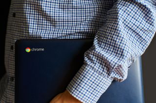 Man in checked shirt holding a chromebook under his arm