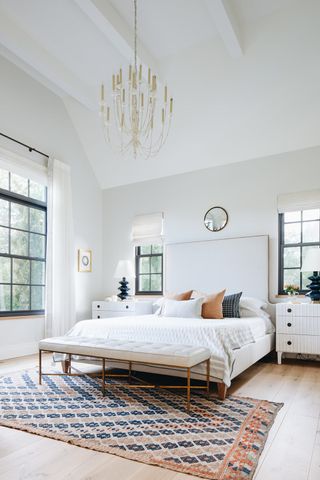 large modern bedroom with chandelier, rug, white bedding and bench seat