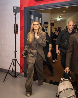 Jennifer Lopez wears a brown blazer, brown button-down shirt, black clutch, brown pants, and platform heels.