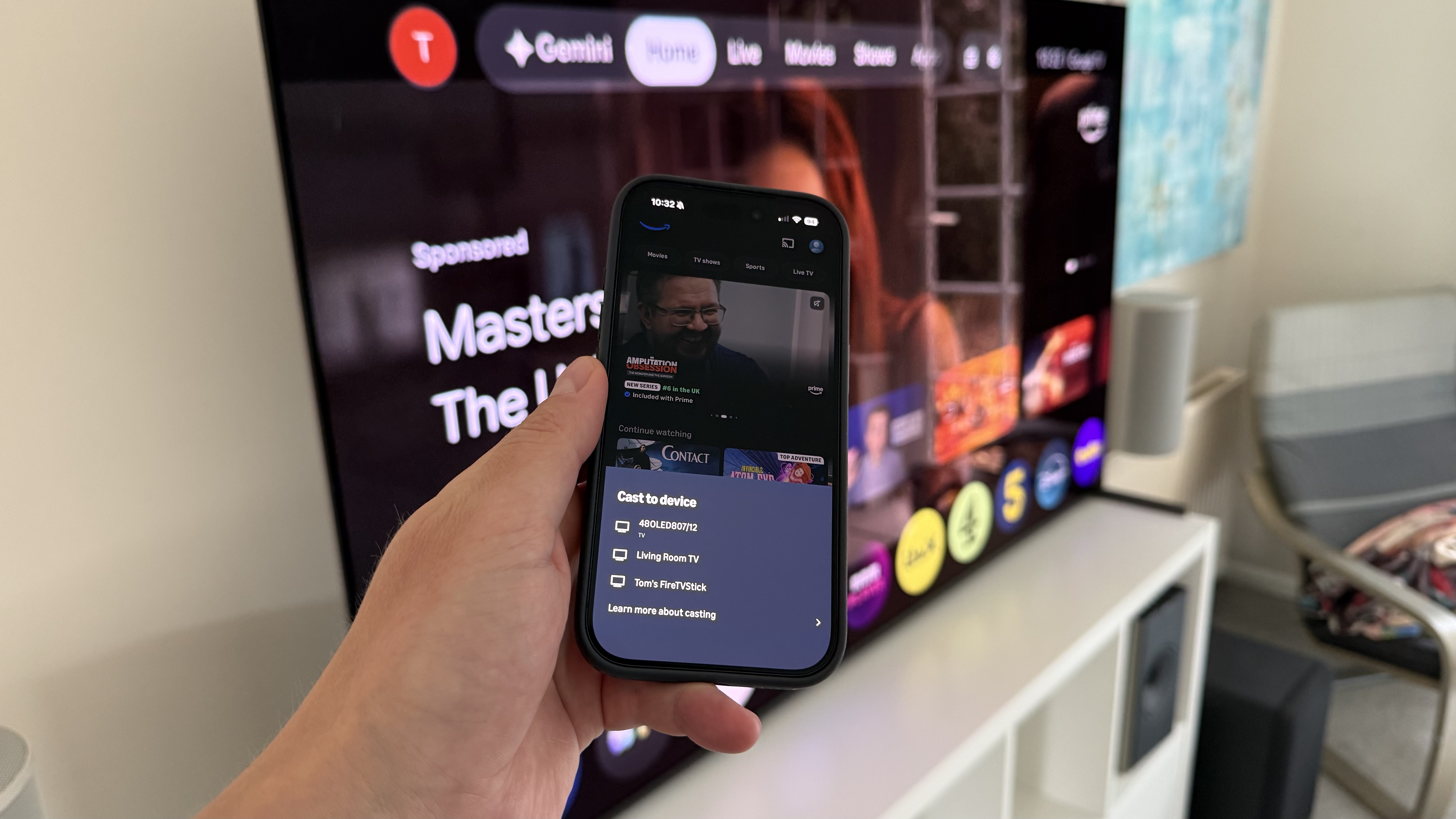 A photo of an iPhone being held in front of a TV. On the phone screen is the Google Cast menu with a list of devices.