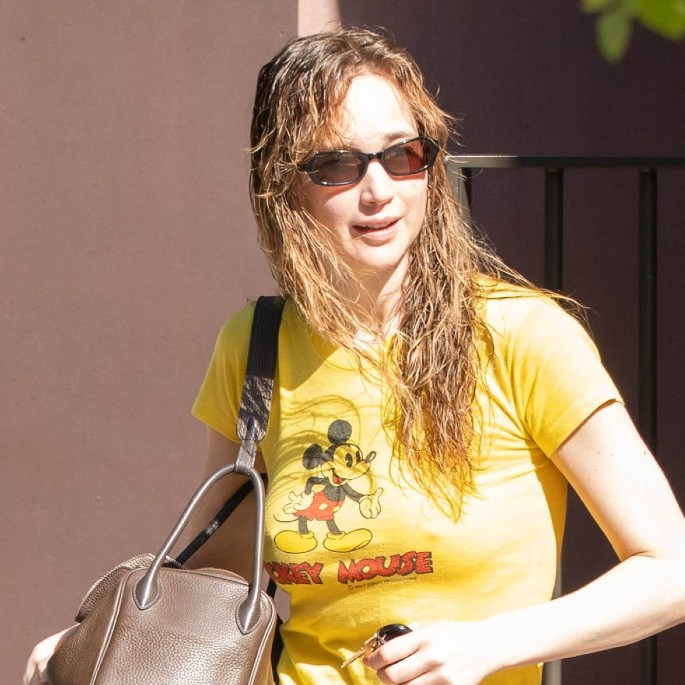 Jennifer Lawrence outside wearing a yellow T-shirt and red track pants 