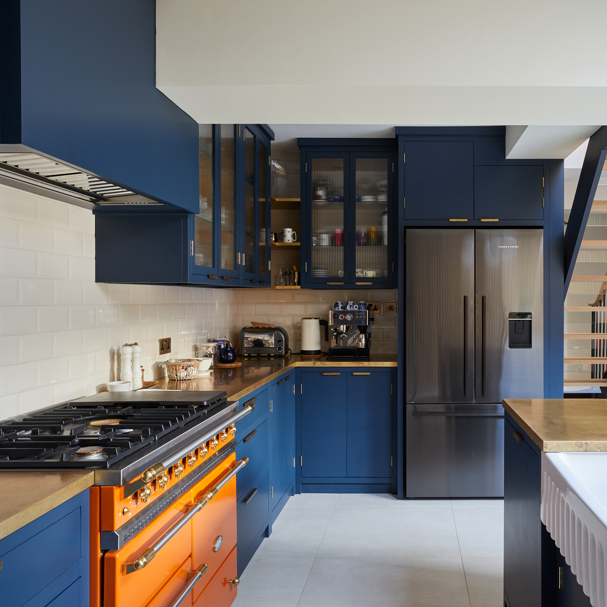 a dark blue kitchen with reeded glass cabinet doors and a bright orange range cooker