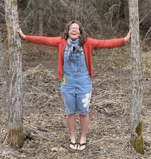 woman wearing dungarees and a red cardigan standing between two trees
