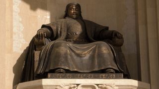 A statue of Genghis Khan sitting on a chair or throne. He is wearing regal robes and a hat.