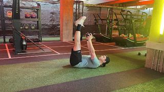 Personal trainer at Gymbox Aaron Cook performs a dumbbell toe touch