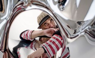 Ron Arad looking through a shiny metallic structure.