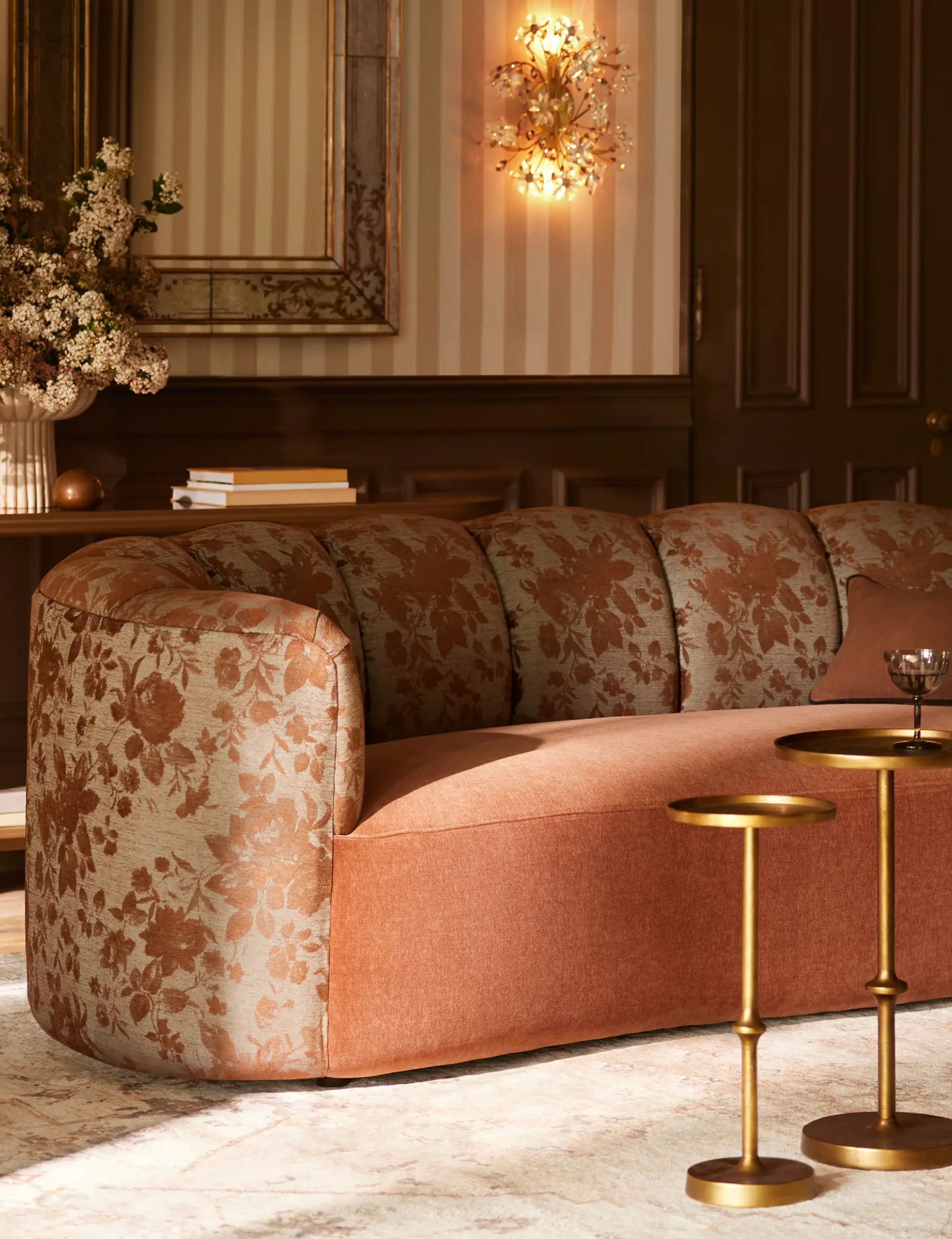 Arhaus' Amira Sofa in Cinnamon pictured in an opulent neutral living room with striped wallpaper and nested brass cocktail tables.