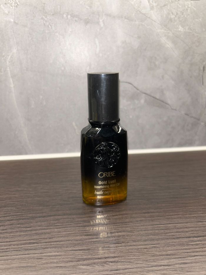 The Oribe Gold Lust Nourishing Hair Oil on the side of a marble bathroom