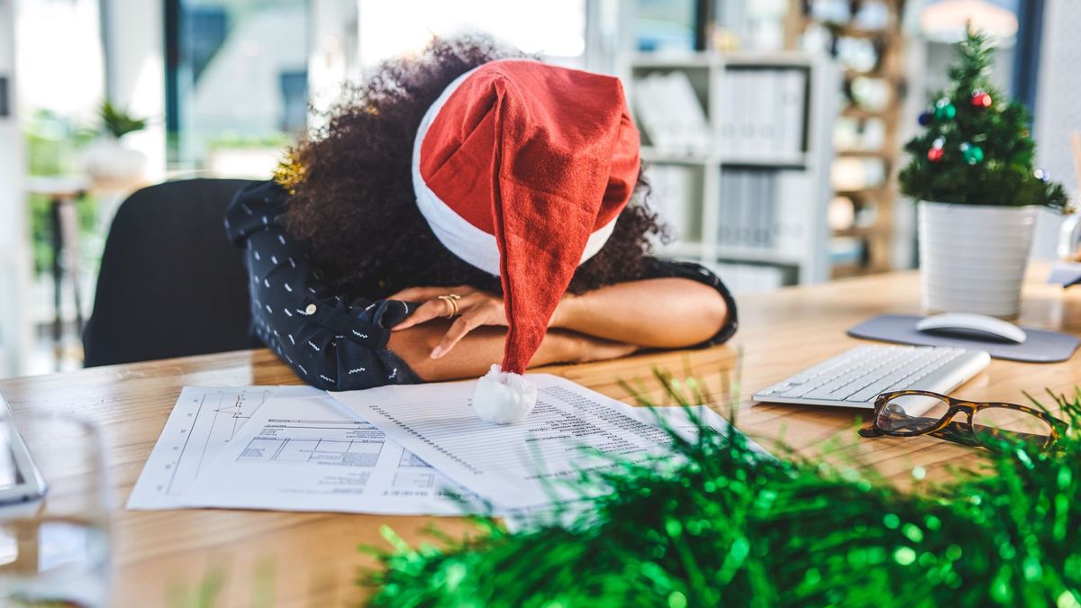 An employee at their desk wearing a festive hat with their head lying on their arms