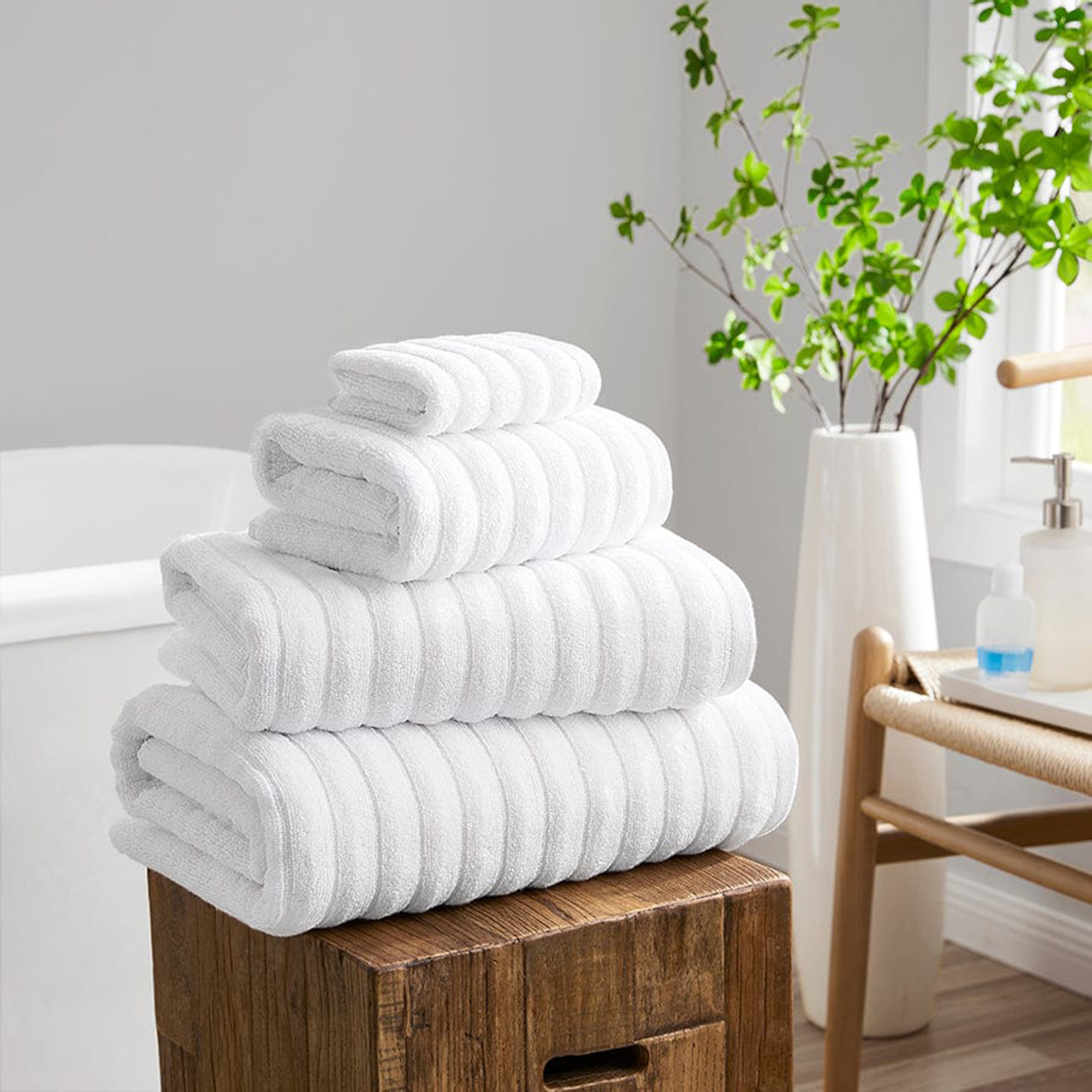 DUSK white towels in a pile on a wooden stool next to a bath