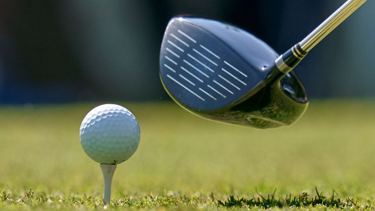 A close up of a driver behind a golf ball teed up