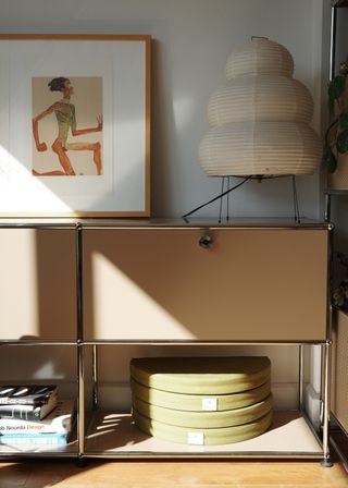 Neutral side cabinet with open shelving on the bottom. there are two folded green floor cushions stack on top of each other