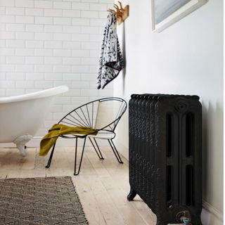 vintage bathroom radiator, pale wood panelled flooring, white bathtub and black wired chair