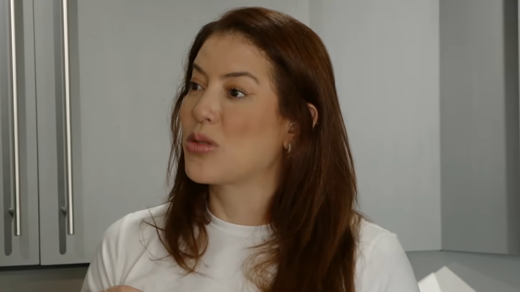 Paula wearing a white t-shirt and lecturing Thomas on the rules of the apartment.