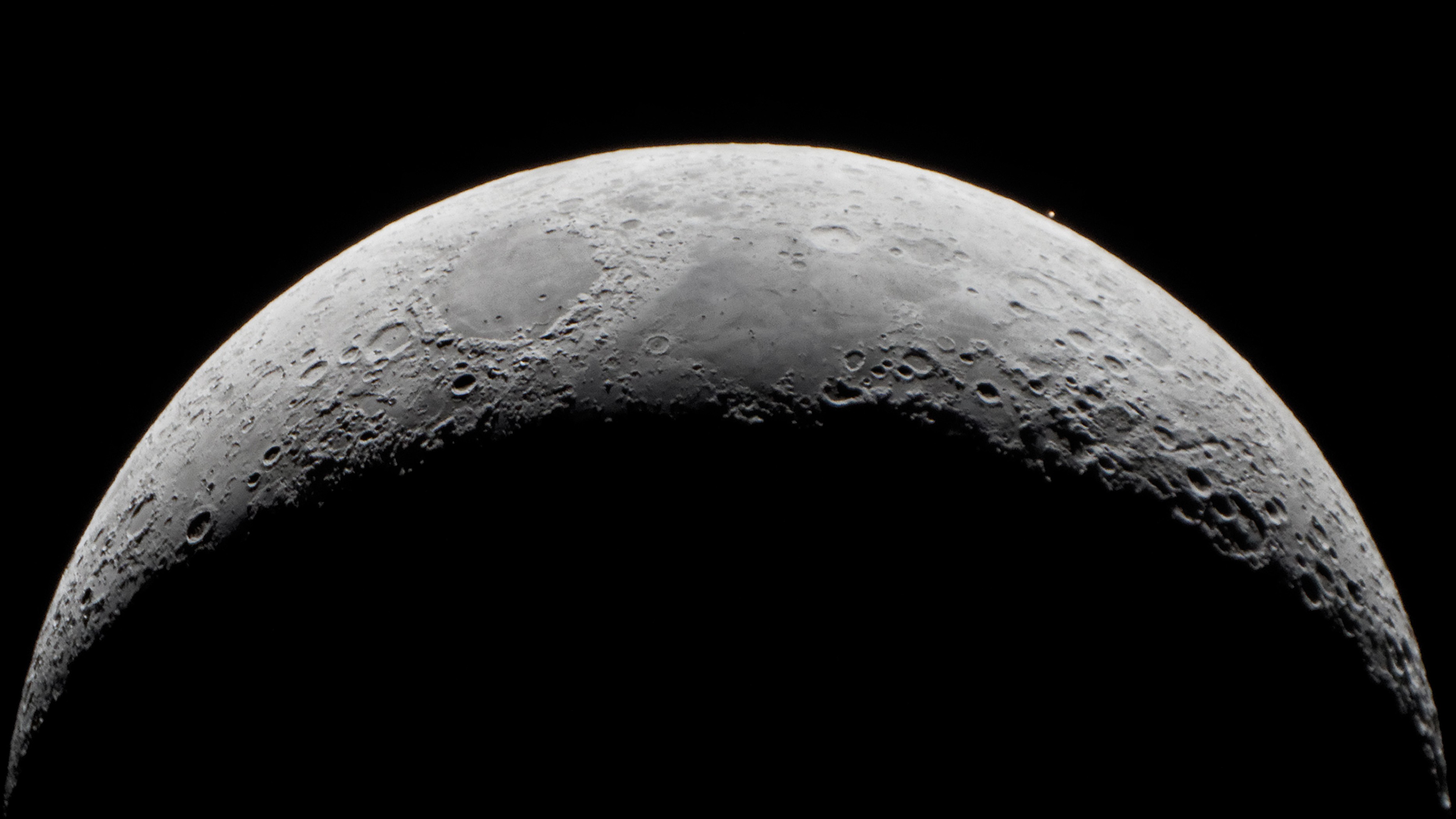 close up view of the moon and toward the upper right of the moon a tiny dot of rusty red light - Mars