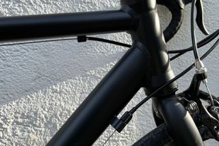 A close up of the Brand X Road Bike external cable and mounts on the front triangle of the bike with a white wall in the background