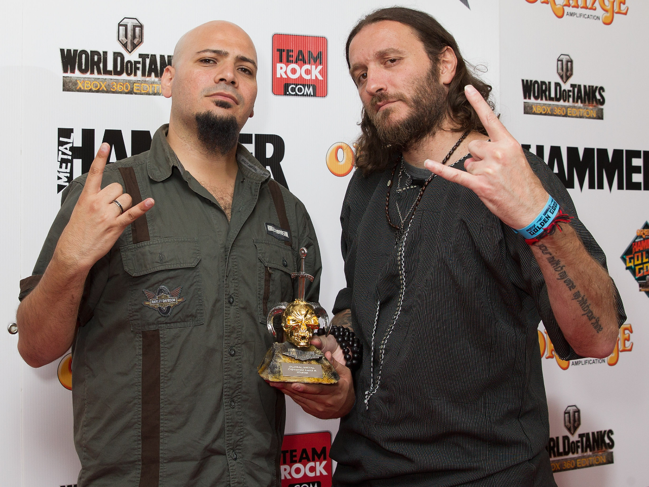 Two men holding an award shaped like a ram's skull and doing the sign of the horns