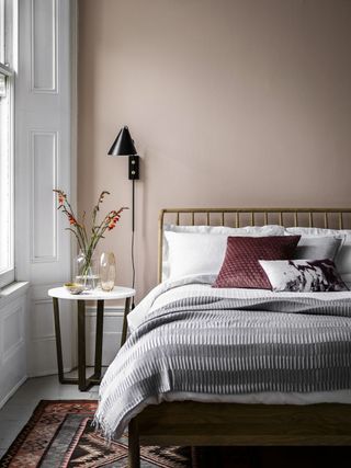 A bedroom with dusty pink wall decor, white bedside table and wooden headboard decor