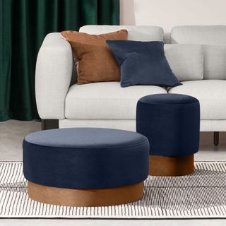 Brown and blue scatter cushions on top of white couch on floor with black and white rug next to navy and cinnamon pouffe