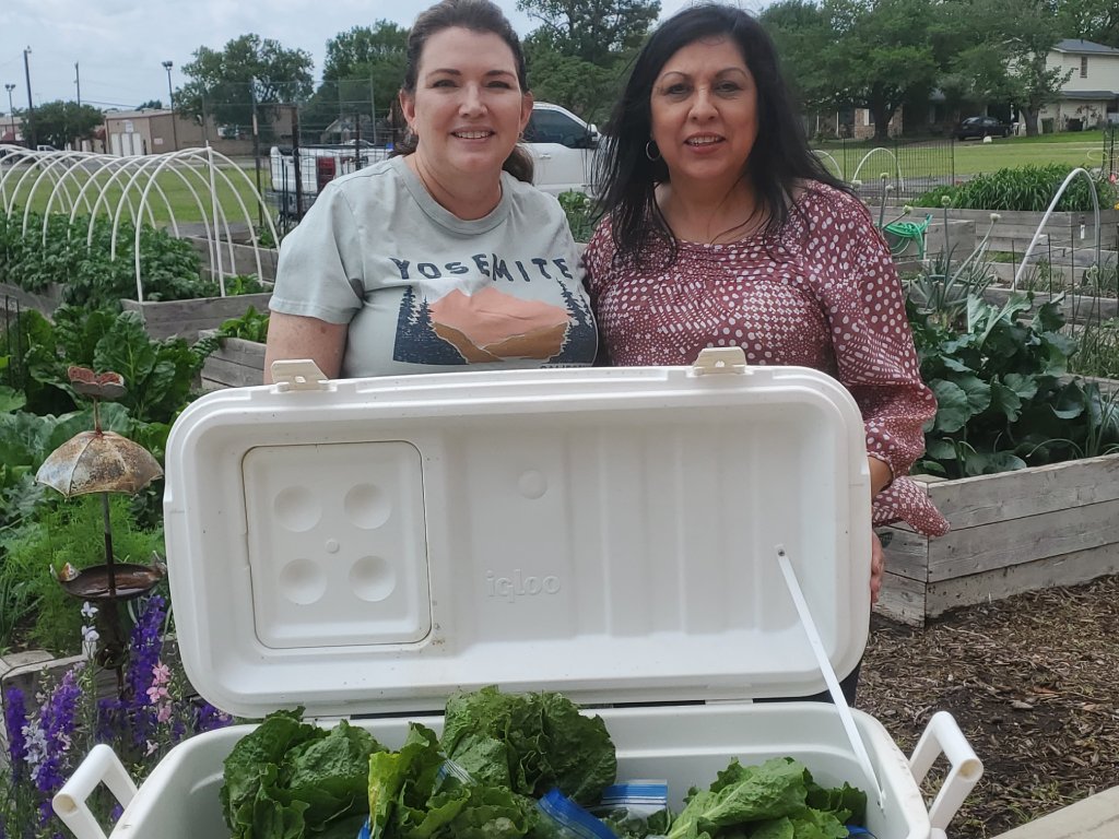 Two smiling women next to a cooler of fresh produce
