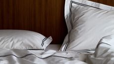 close up of piped pillowcases and sheets with a timber headboard