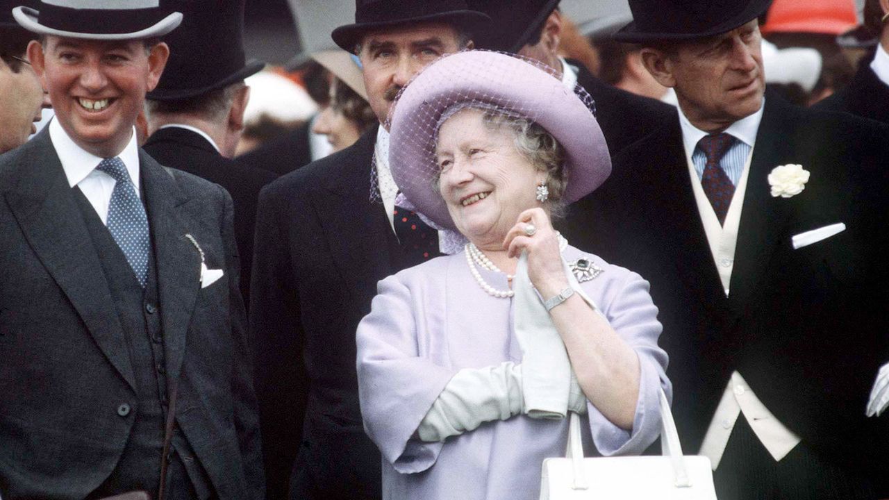 The Queen Mother wearing a lavender coat and hat laughing next to Prince Philip and men in top hats