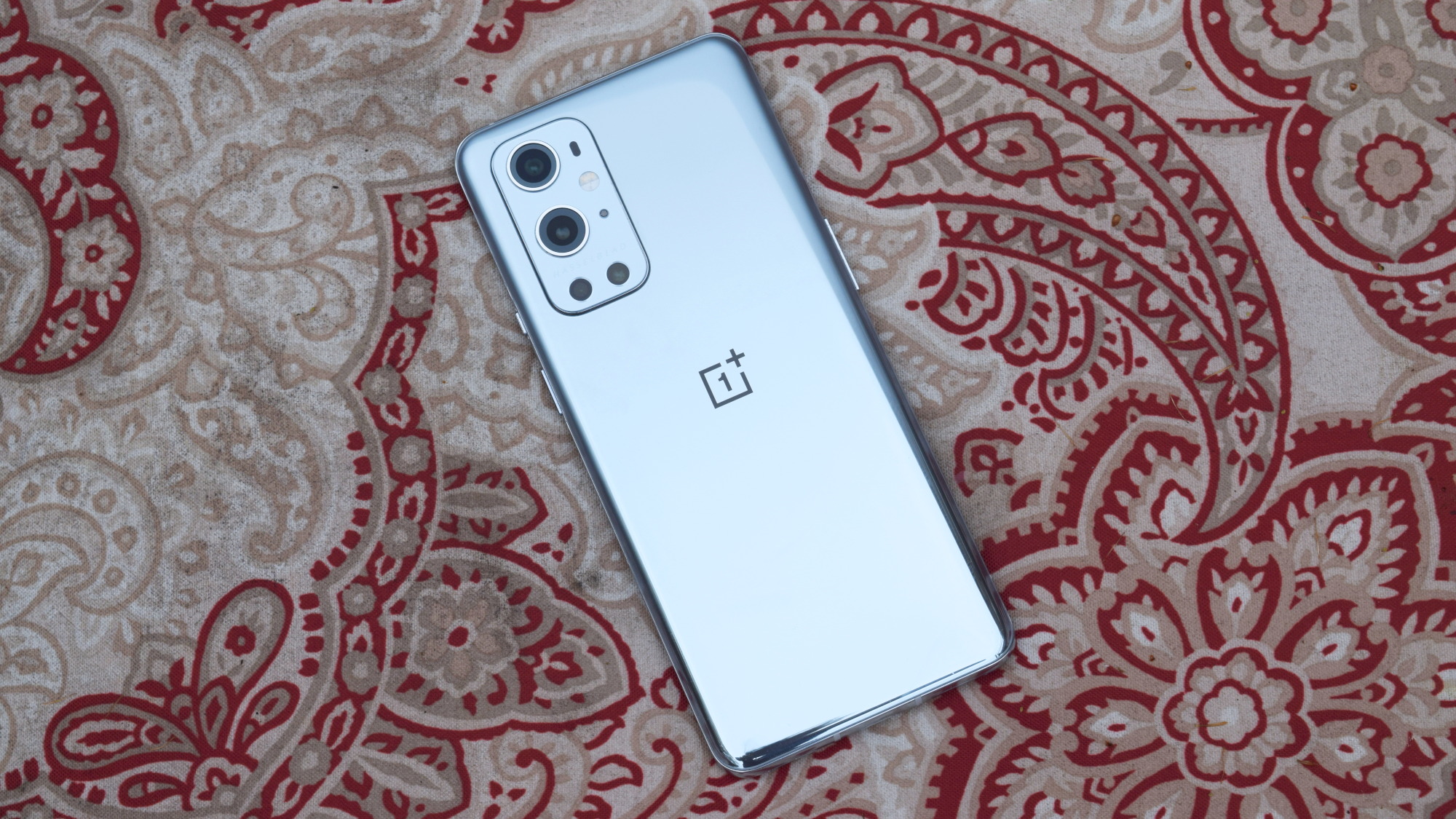 A silver OnePlus 9 Pro, lying face-down on a patterned carpet