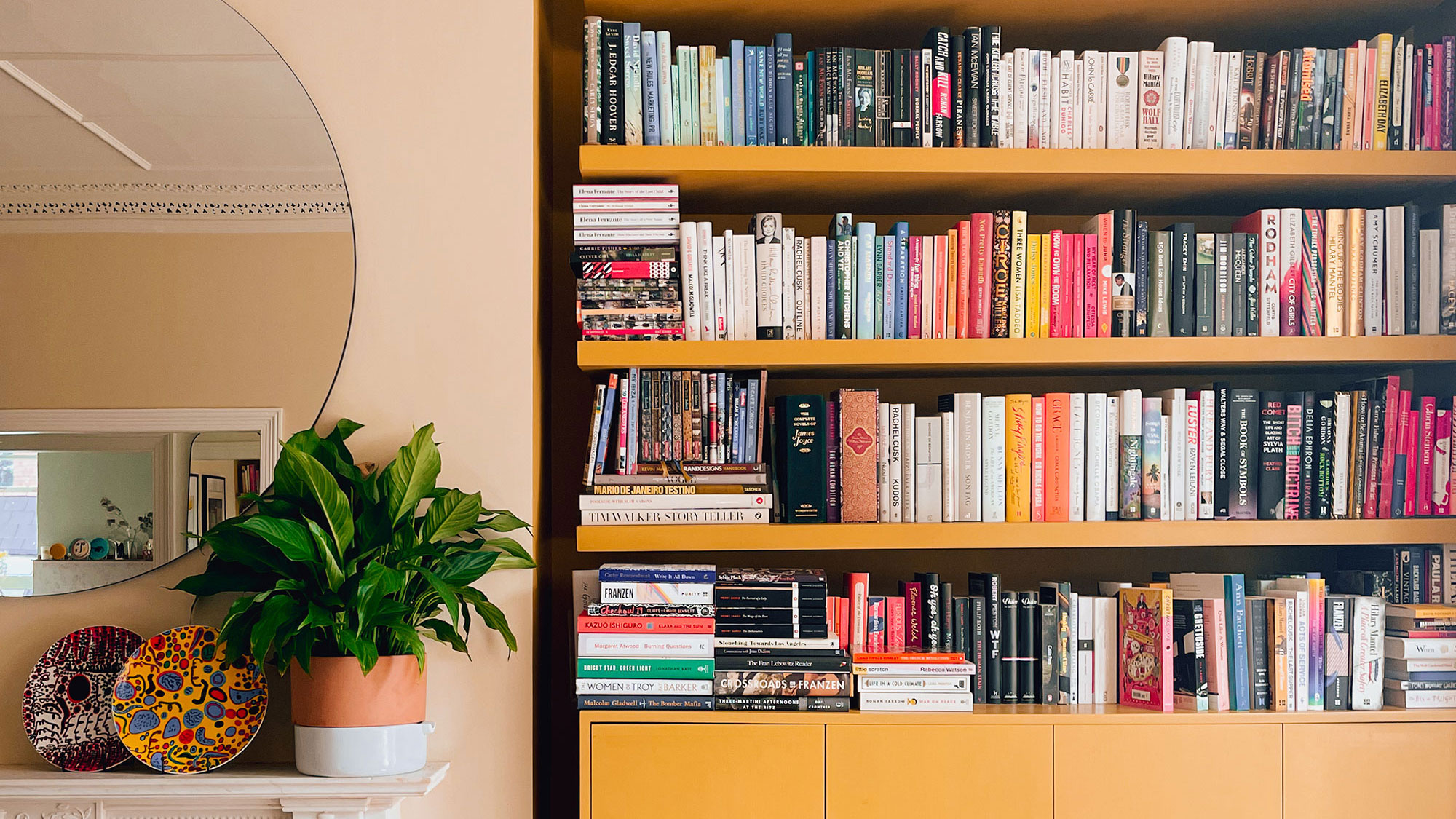 Yellow bookcases beside fireplace and round mirror
