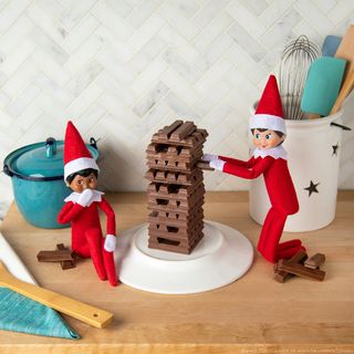 Elf on the Shelf ideas – two elves building a chocolate tower on the kitchen counter made out of KitKat bars
