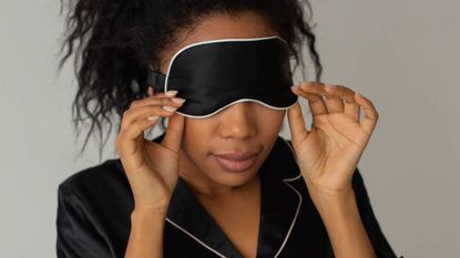 Woman putting on a black silk face mask, wellness tips