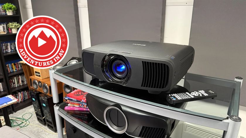 The Epson EH-LS9000 projector, photographed on a rack in a home cinema room. In the corner of the image is a red badge that says &#039;Adventures in AV&#039;.