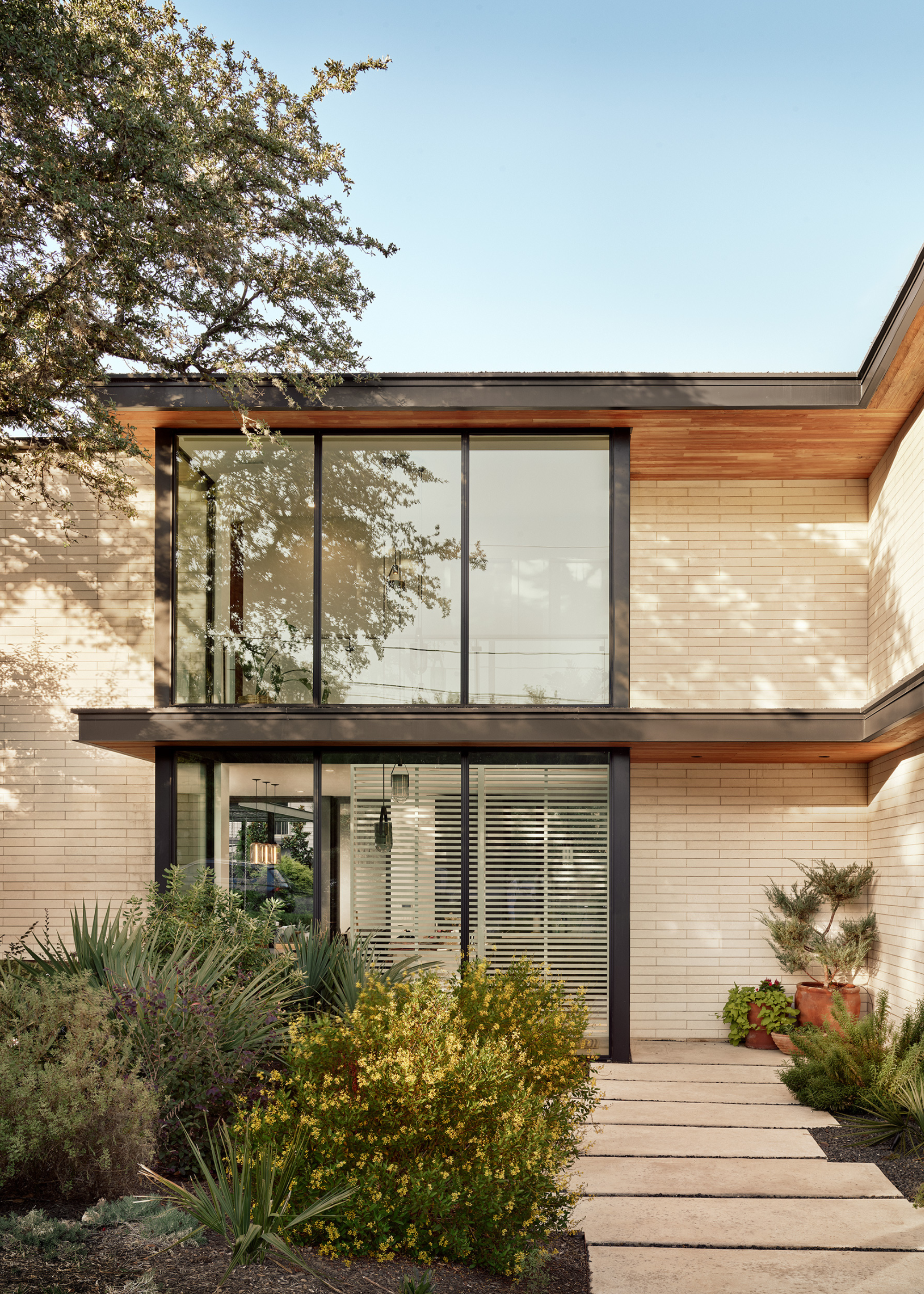 A two-storey home with cream stone paving on flat stepping stones leading through a garden