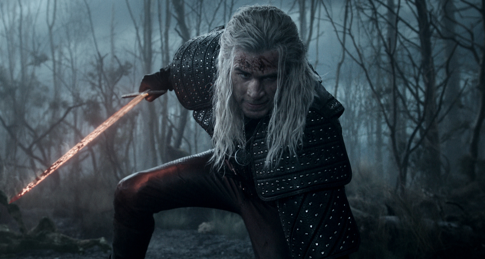 liam hemsworth as geralt of rivia wielding a red glowing sword while crouching down in the witcher season 4