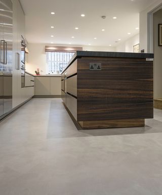 pale grey microcement floor in kitchen with large dark veneer wood kitchen island