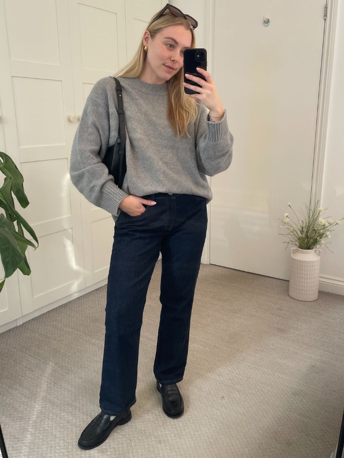 Woman wears grey sweater, blue jeans and black loafers