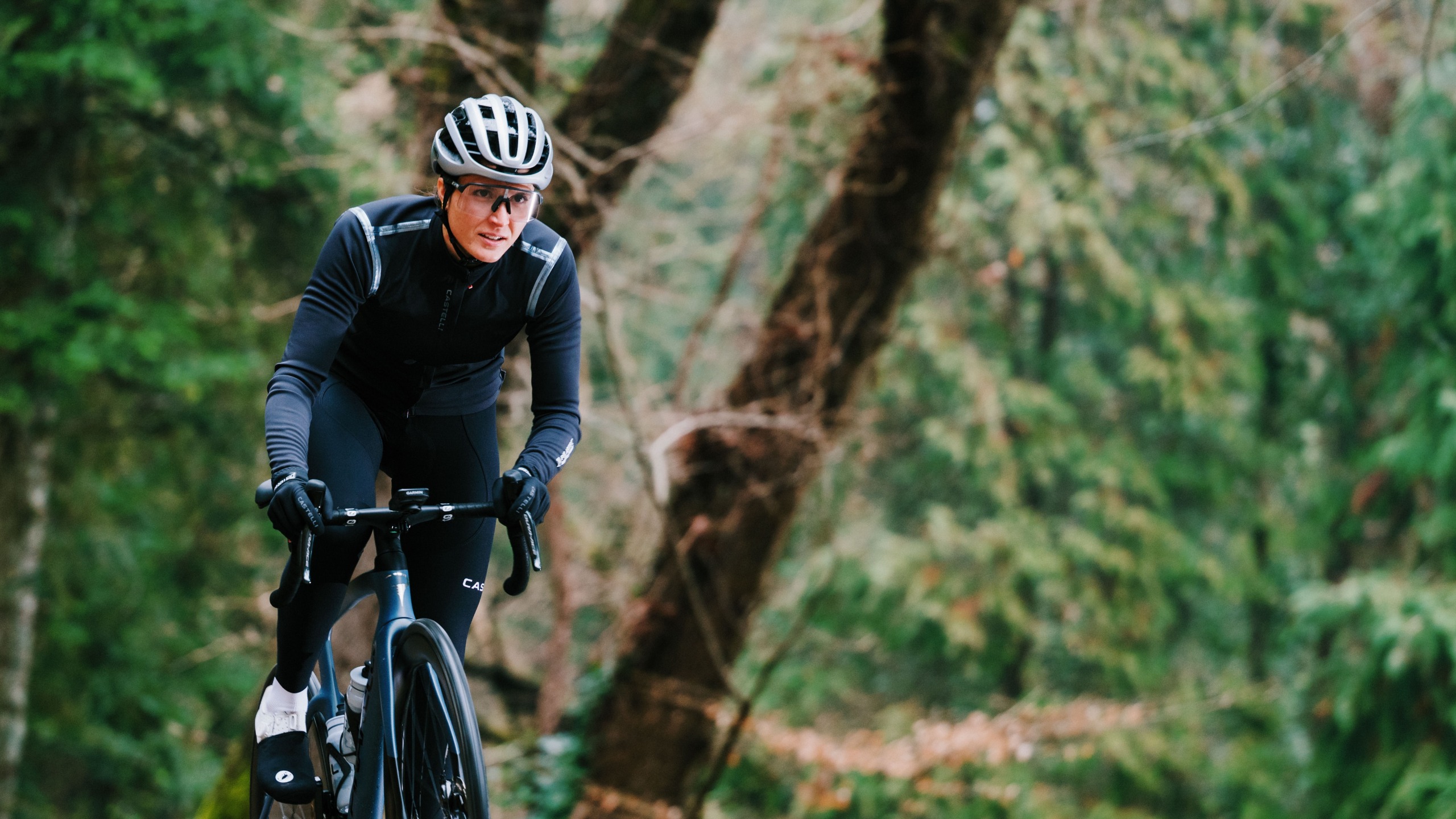 A woman rides up a climb on the hoods wearing the Castelli Perfetto 4