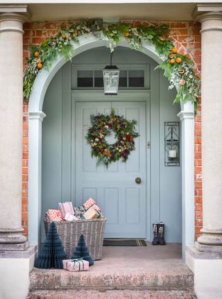 Blue door and archway with Christmas garland and wreath, presents in baskets on step