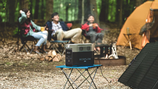 EcoFlow DELTA mini portable power station with solar panel sitting on table at campsite, three campers in background