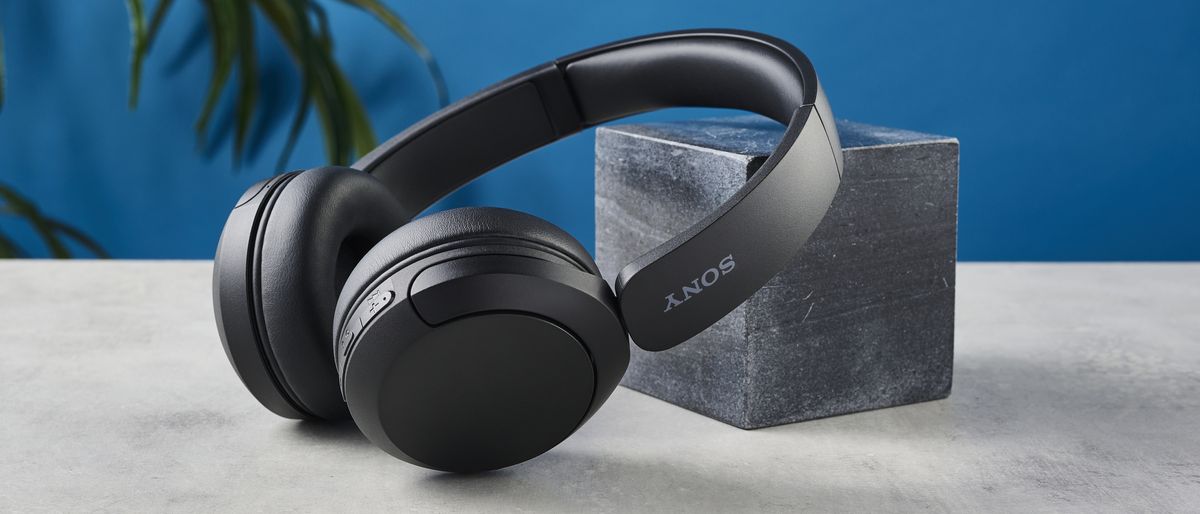 A photo of the Sony WH-CH520 wireless over ear headphones, resting on a stone surface against a black marble block and a blue background