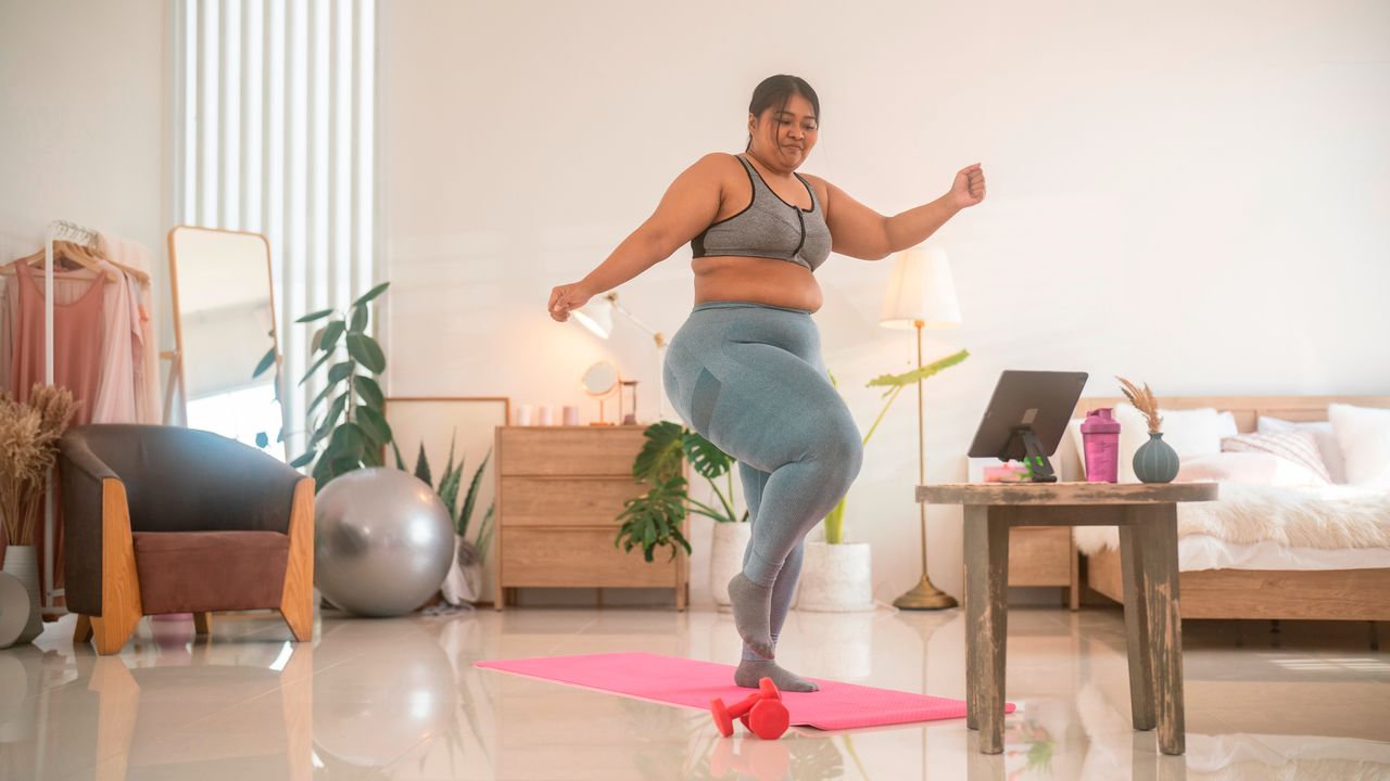 Woman exercising in front of tablet on exercise mat in domestic setting wearing sportswear