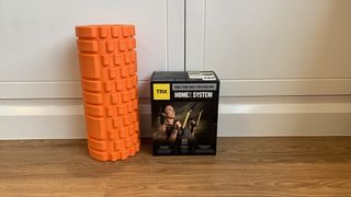 TRX Home2 System suspension trainer review: The Home2 kit pictured on teak wooden flooring and sat next to an orange foam roller