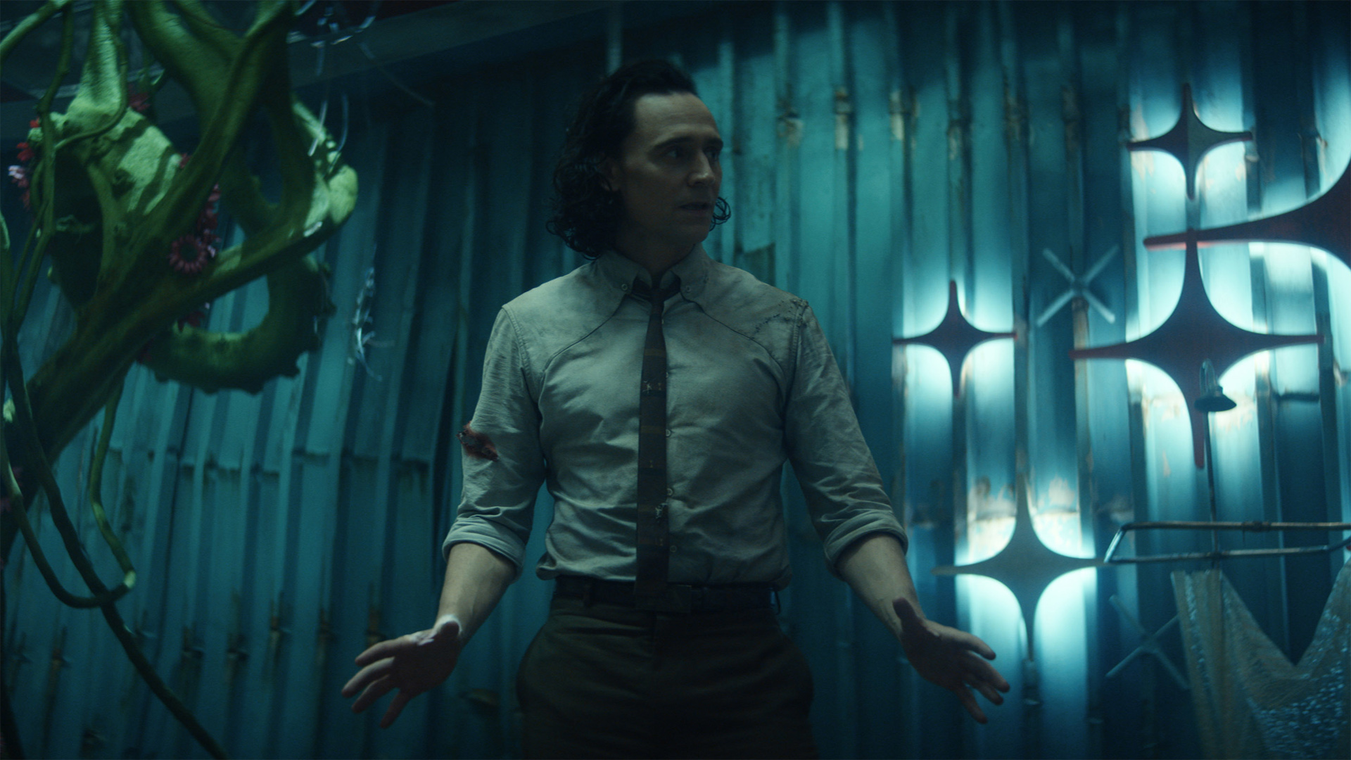 Tom Hiddleston as Loki, standing in a dark room wearing a shirt and tie