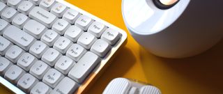 Lofree Flow mechanical wireless keyboard photograph showing top right corner of laptop with other similarly colored desk accessories.